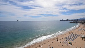 Una spiaggia con cielo sereno, mare calmo e una città sullo sfondo.