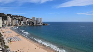 Paesaggio costiero con spiaggia, grattacieli e cielo sereno.