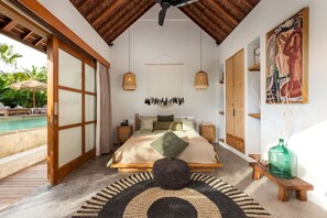 Ein Schlafzimmer mit Bett, Nachttischen, einer Pendelleuchte, einem Gemälde und Blick auf einen Pool.