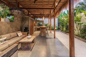 A covered outdoor seating area with a sofa, a wooden table, and a hanging light fixture.