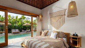 Ein Schlafzimmer mit einem großen Bett, einem hölzernen Kopfteil, einem Nachttisch, einer Pendelleuchte und Blick auf einen Außenpool.