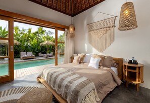 Ein Schlafzimmer mit einem großen Bett, einem hölzernen Kopfteil, einem Nachttisch, einer Pendelleuchte und Blick auf einen Außenpool.
