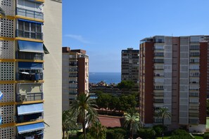 Ein Hochhaus mit mehreren Balkonen, Blick auf das Meer und umliegender Bepflanzung.