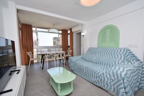 Ein modernes Wohnzimmer mit einer Couch, einem Esstisch mit Stühlen, einem Fernseher und einem Fenster mit Vorhängen.