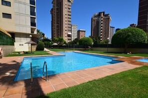 A rectangular swimming pool with metal ladders, surrounded by a grassy area and a paved walkway. - Torre Ipanema 9D in Benidorm (Benidorm)