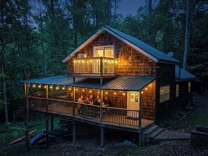 Une cabane en bois à deux étages, dotée d’un balcon et entourée d’arbres.