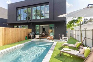 Una casa moderna de dos pisos con piscina, mobiliario exterior y zona de barbacoa.