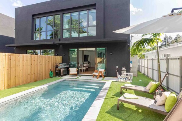 Una casa moderna de dos pisos con piscina, mobiliario exterior y zona de barbacoa.