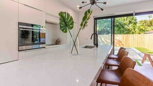 Una cocina moderna con horno empotrado, un comedor con una mesa grande y sillas, y un amplio ventanal con vistas a un jardín.