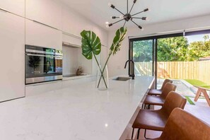 Una cocina moderna con horno empotrado, un comedor con una mesa grande y sillas, y un amplio ventanal con vistas a un jardín.
