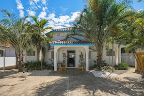 A house with a tiled roof, a front door, two wicker chairs, and surrounding palm trees. - Spacious 12-bedroom resort with AC in excellent Cabarete (Cabarete)