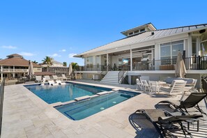 Ein Swimmingpool mit Liegestühlen, eine überdachte Terrasse und ein großes Haus mit mehreren Etagen und Balkonen.