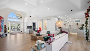 A spacious living area with a white sofa, coffee table, and decorative pillows. There is a large window with a view of greenery outside. - Luxury Waterfront Retreat with Gulf Access, Pool & Sunset Views (Bonita Springs)