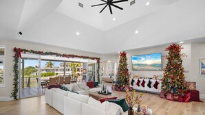 A spacious living room with a white sofa, two Christmas trees, and a balcony with a view. - Luxury Waterfront Retreat with Gulf Access, Pool & Sunset Views (Bonita Springs)