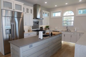 A modern kitchen with stainless steel appliances, white cabinetry, and a central island with a sink and faucet. - Luxury Waterfront Retreat with Gulf Access, Pool & Sunset Views (Bonita Springs)