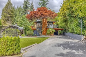 A modern house with a large tree in front, a covered porch, and a well-maintained lawn. - Modern Mid-Century Home - Solarium, Deck and Jacuzzi (North Vancouver)