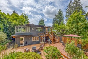 A two-story house with a deck, surrounded by trees.