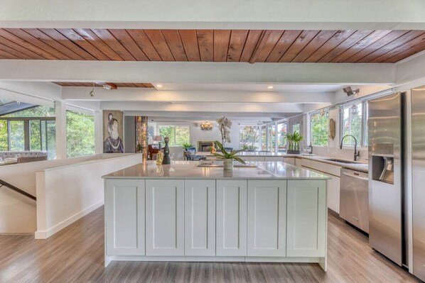 A spacious kitchen with a large island, wooden ceiling, and ample natural light.