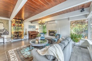 Ein großzügiges Wohnzimmer mit großem Fenster, Kamin, Klavier und Barbereich.