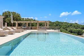 A swimming pool with lounge chairs and a pergola, surrounded by greenery and a clear sky. - Thaloria Villa (Rethymno)