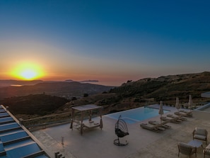 A rooftop pool area with lounge chairs, a table, and a chair, overlooking a hilly landscape during sunset. - Thaloria Villa (Rethymno)