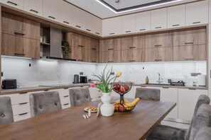 A modern kitchen with wooden cabinets, a marble countertop, and a dining area with a wooden table and grey upholstered chairs. - Thaloria Villa (Rethymno)