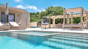 A pool area with lounge chairs, a hanging chair, and a pergola. - Thaloria Villa (Rethymno)