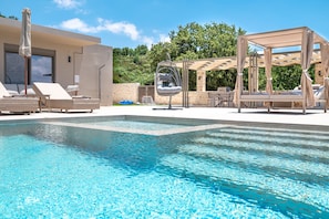 A pool area with lounge chairs, a hanging chair, and a pergola. - Thaloria Villa (Rethymno)