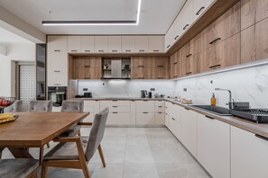 A modern kitchen with wooden cabinets, a marble countertop, and a dining area with a wooden table and chairs. - Thaloria Villa (Rethymno)
