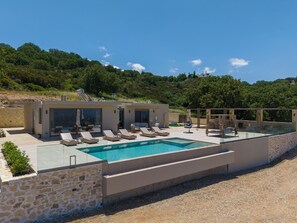 A modern poolside area with lounge chairs, a glass-enclosed pool, and a stone wall. - Thaloria Villa (Rethymno)