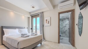 A modern hotel room with a large bed, a bathroom with marble walls, and a view of the outdoors. - Thaloria Villa (Rethymno)