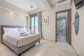 A modern hotel room with a large bed, a bathroom with marble walls, and a view of the outdoors. - Thaloria Villa (Rethymno)