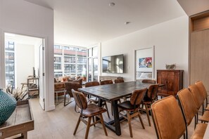 Ein geräumiger Essbereich mit großem Tisch und Ledersesseln, einem wandmontierten Flachbildfernseher und Blick auf die Stadt durch große Fenster.