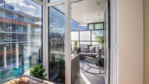 Ein Balkon mit einer Couch, einem Schaukelstuhl und Blick auf ein Gebäude mit Schwimmbad.