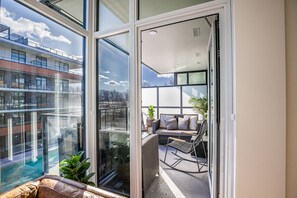A balcony with a sofa, a rocking chair, and a view of a building with a swimming pool. - Beautiful 2 Bedroom at Caban (Kelowna)