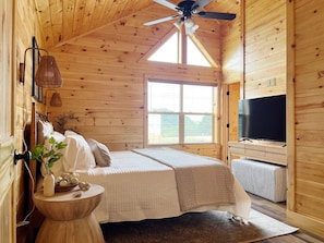 Ein Schlafzimmer einer Holzhütte mit Bett, Nachttisch, Fernseher und Fenster.