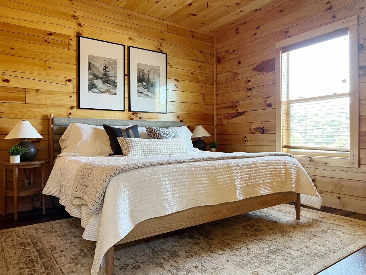 Een slaapkamer met houten lambrisering, een bed, twee ingelijste foto's, twee bedlampen en een raam.
