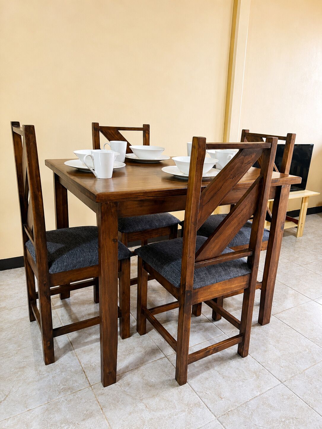 A wooden dining table with chairs, a TV, and a laptop on a stand.