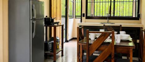 A kitchen with a refrigerator, a dining table with chairs, a window with bars, and an air conditioning unit.