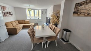 A modern living room with a sofa, dining table, and chairs, a clock, and a window with natural light. - Modern | Central | Park Free | Northants (West Northamptonshire)