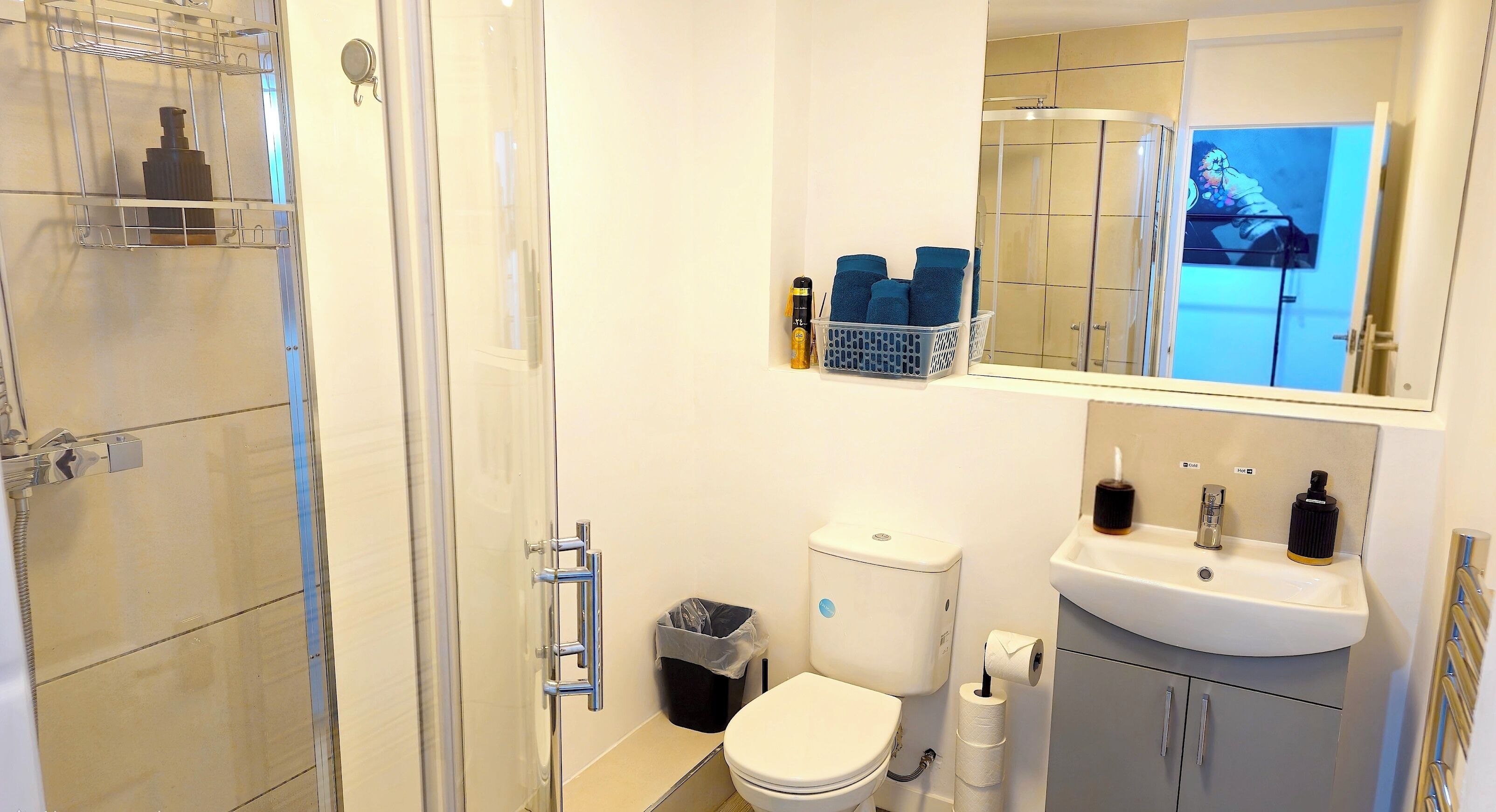 Un baño con cabina de ducha de vidrio, inodoro, lavamanos y espejo que refleja la zona de la ducha.
