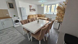 A modern kitchen with a built-in washing machine, a dining area with a white table and brown chairs, and a corner seating area with a sofa. - Modern | Central | Park Free | Northants (West Northamptonshire)