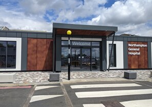 A hospital entrance with a 'Welcome' sign, a clear sky, and a tiled pavement. - Modern | Central | Park Free | Northants (West Northamptonshire)