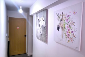 A hallway with a wooden door, a light fixture, and two artworks on the wall.