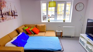 Ett modernt sovrum med en säng, en soffa, ett litet bord, ett element och en tv.