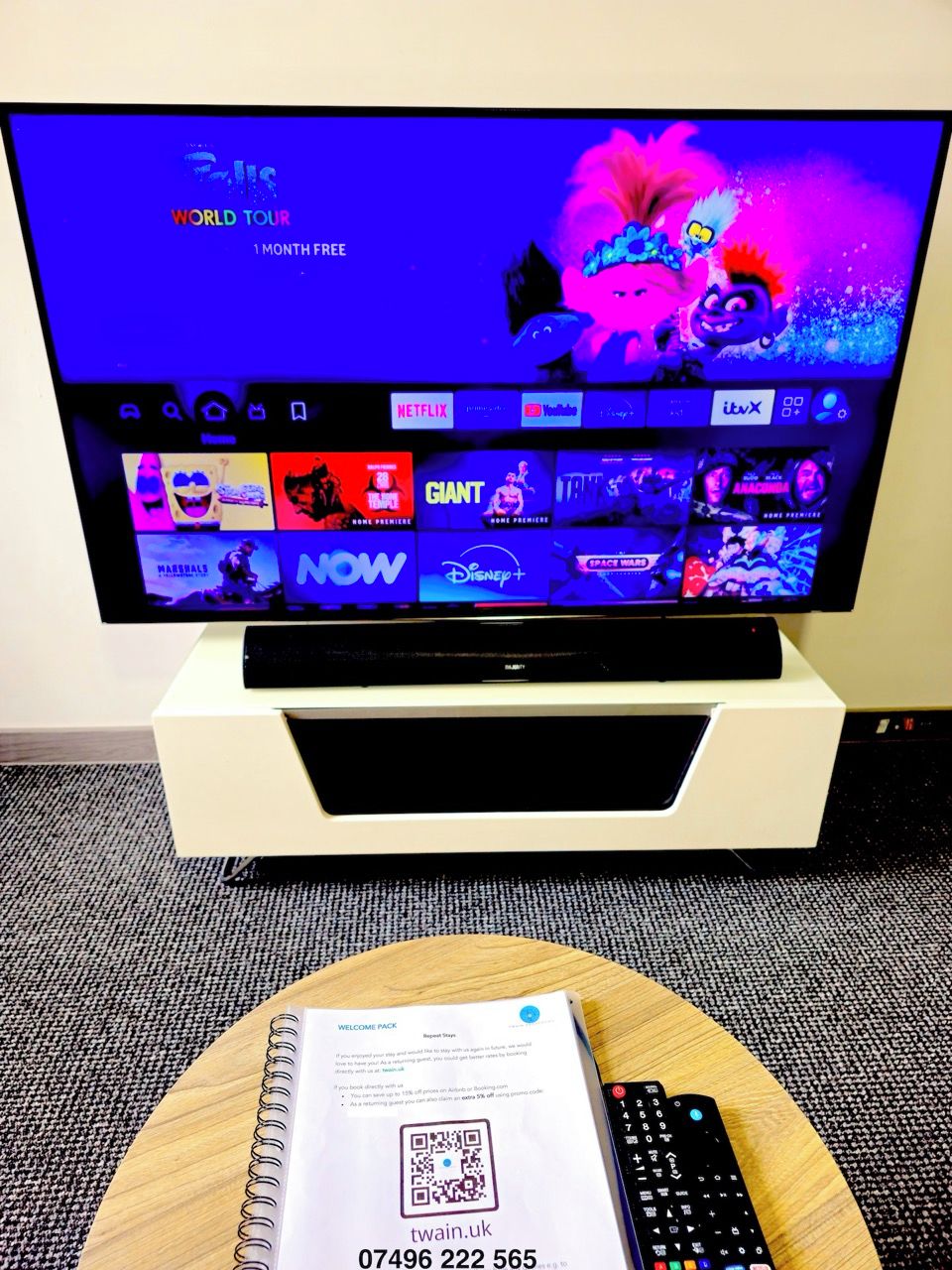 A television on a stand with a remote control and a welcome pack on a table.