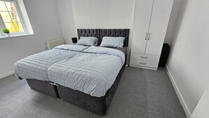 A bedroom with a bed, a wardrobe, a radiator, and a window with a plant. - Modern | Central | Park Free | Northants (West Northamptonshire)