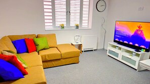 Un saló amb un sofà, una televisió, un rellotge i un radiador.