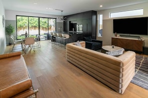 Una sala moderna con un sofá, un comedor con sillas, una zona de cocina y un televisor grande.