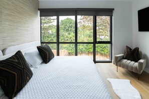 Un dormitorio con una cama grande, un sofá y vistas a la vegetación a través de amplias ventanas.
